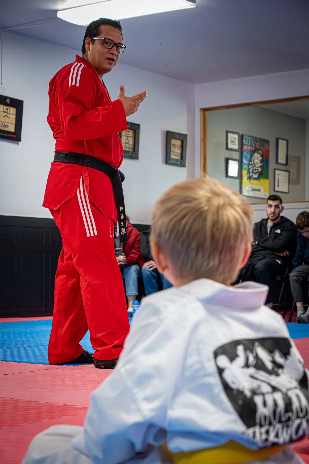 Instructeur de HLD Taekwondo s'adressant à sa classe, entouré de certificats et de repères de progression